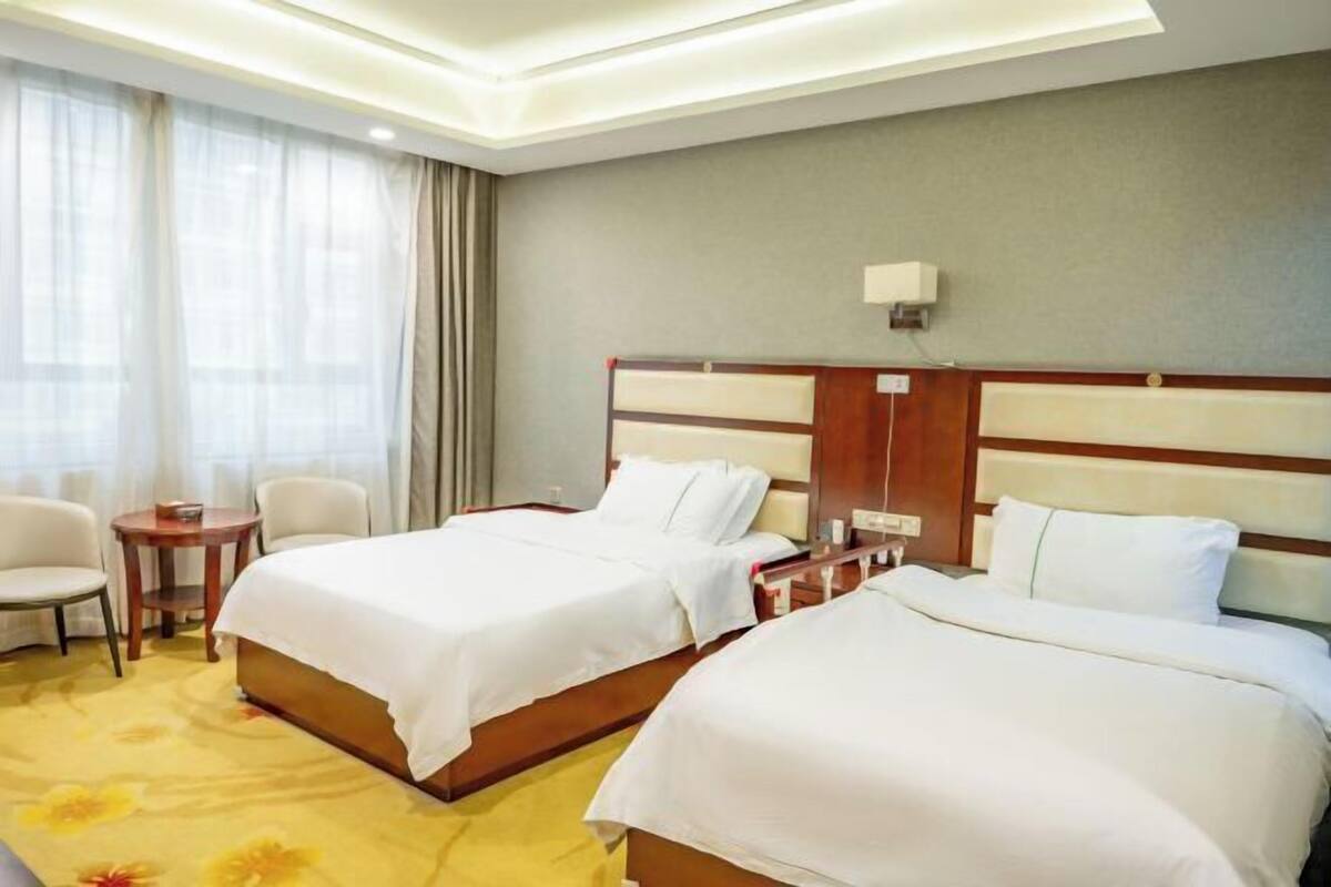 A hotel room with two beds, a small table, chairs, and a window with curtains.