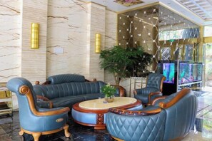 A lobby with a sectional sofa, armchairs, a coffee table, and a large plant. - Yajia Hotel (Kaiyang)