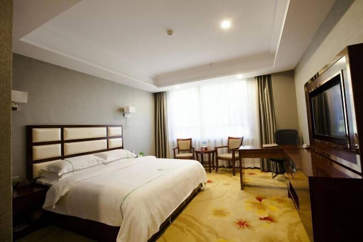 A hotel room with a large bed, a desk with two chairs, a television, and a window with curtains.
