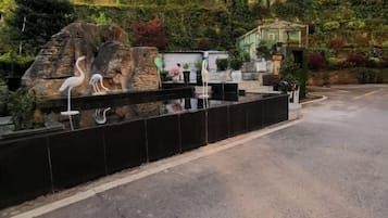 Un área ajardinada con una fuente, una estructura de piedra y un pequeño edificio con techo verde.