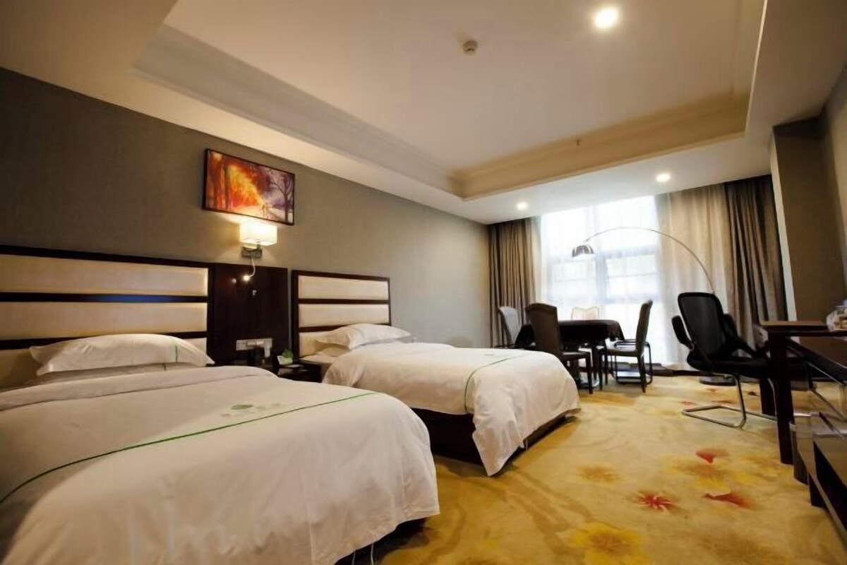 A hotel room with two beds, a desk, a chair, a lamp, and a painting on the wall.