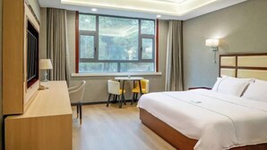 A hotel room with a large bed, a desk, two chairs, a window with curtains, and a wall-mounted lamp. - Yajia Hotel (Kaiyang)