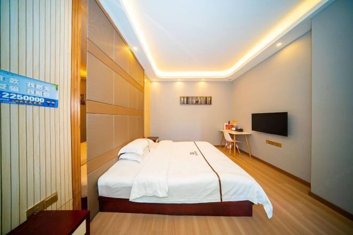 Una habitació d'hotel amb un llit, un escriptori, una cadira, un televisor i un cartell a la paret.