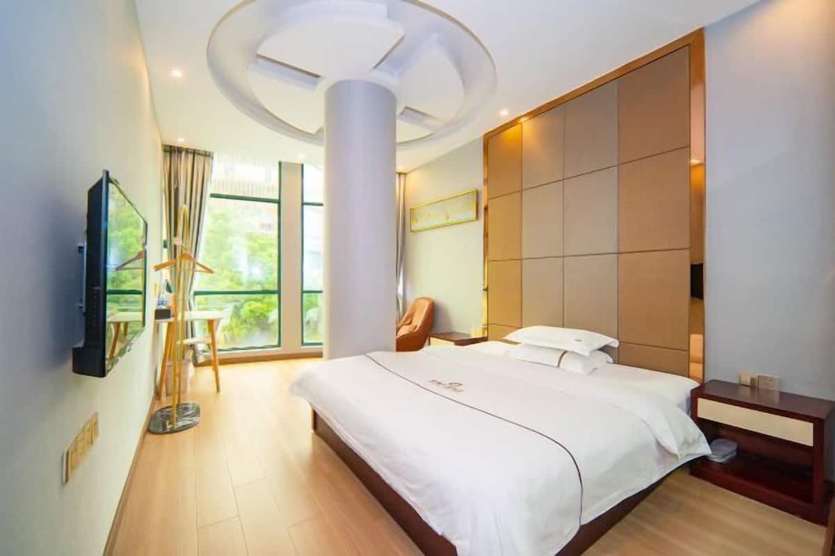 Habitació d'hotel moderna amb un llit gran, televisió de pantalla plana, sòl de fusta i una finestra gran que ofereix vistes a la vegetació.