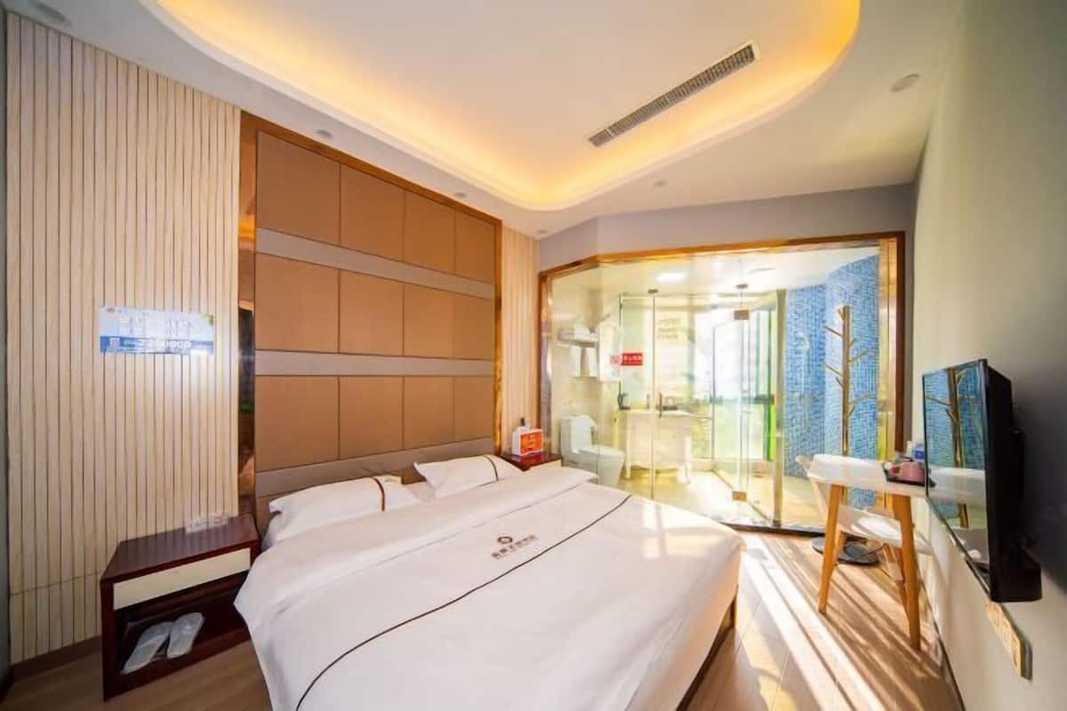 Habitació d'hotel amb un llit gran, una taula de nit, una televisió i una porta de vidre que dona a un bany.