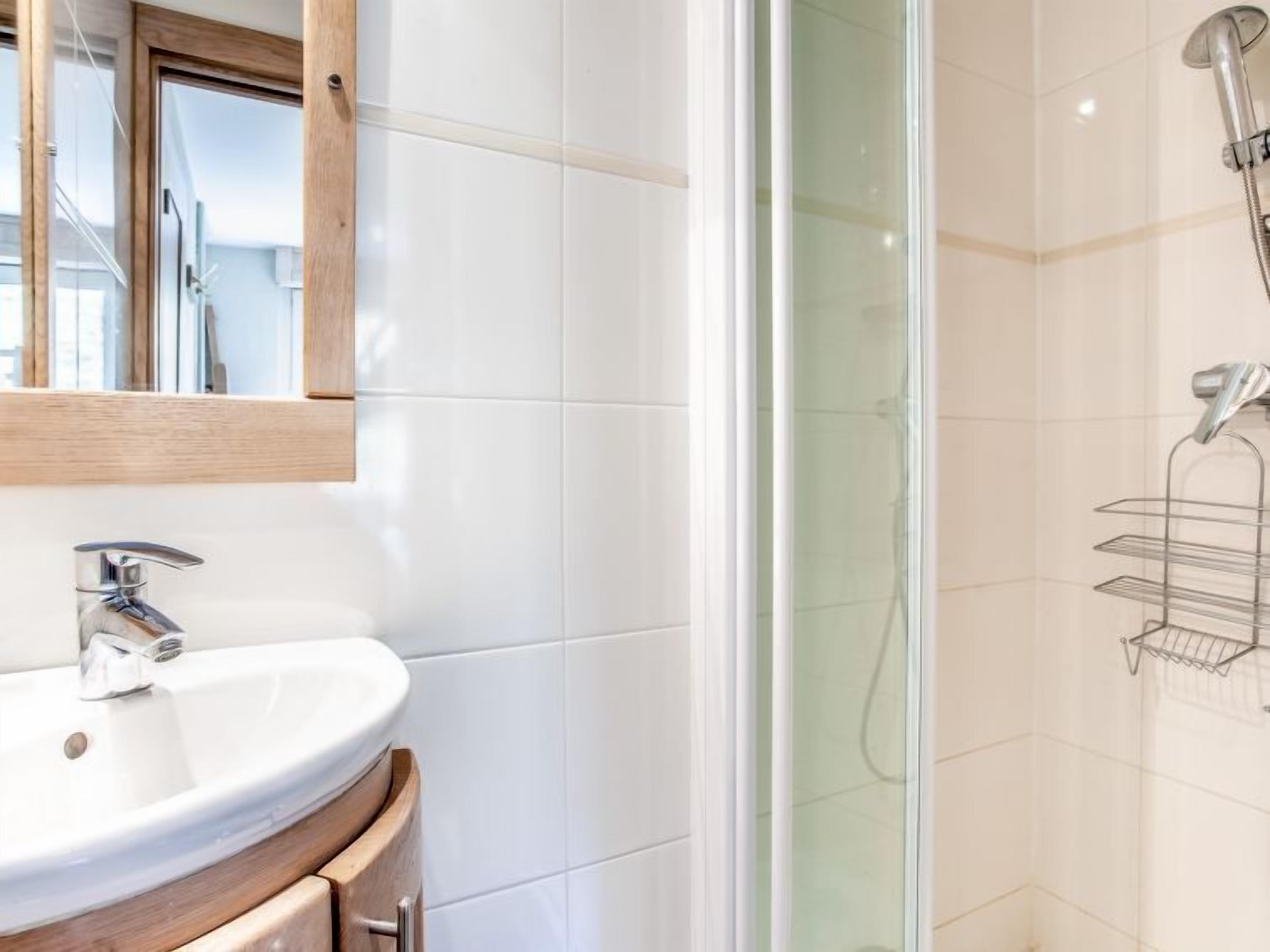 A bathroom with a white sink, a wooden vanity, a glass shower enclosure, and a metal towel rack.
