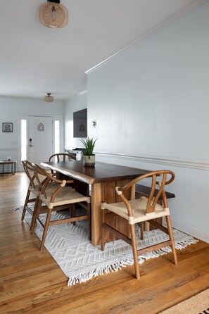 A dining area with a wooden table and chairs, a woven ceiling light, and a white wall. - Modern Boho style Folly beach house -3 blocks from the beach! (Folly Beach)