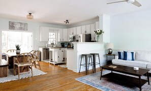 A modern kitchen with white cabinets, stainless steel appliances, and a dining area with wooden chairs and a table. - Modern Boho style Folly beach house -3 blocks from the beach! (Folly Beach)