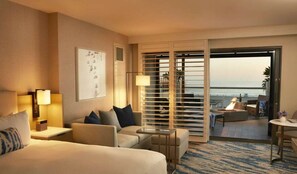 A hotel room with a bed, a sofa, a small table, a lamp, and a view of the ocean through a sliding door. - La Plage Wellness (Santa Monica)