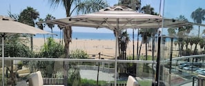 A beach view from a balcony with a glass railing, palm trees, and a beach umbrella. - La Plage Wellness (Santa Monica)