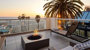 A balcony with a fire pit, lounge chairs, and a view of the beach and ocean at sunset. - La Plage Wellness (Santa Monica)