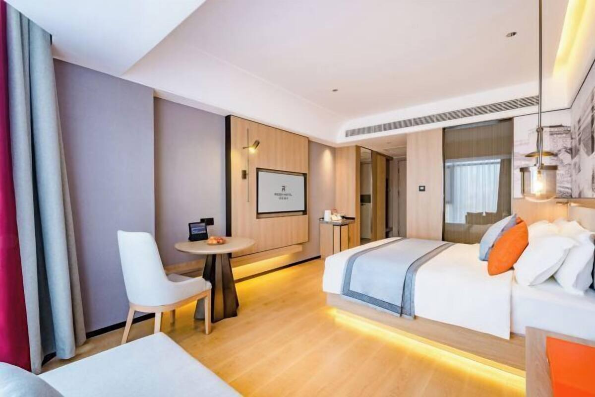 Ett modernt hotellrum med en säng, ett skrivbord, en stol och ett litet bord.