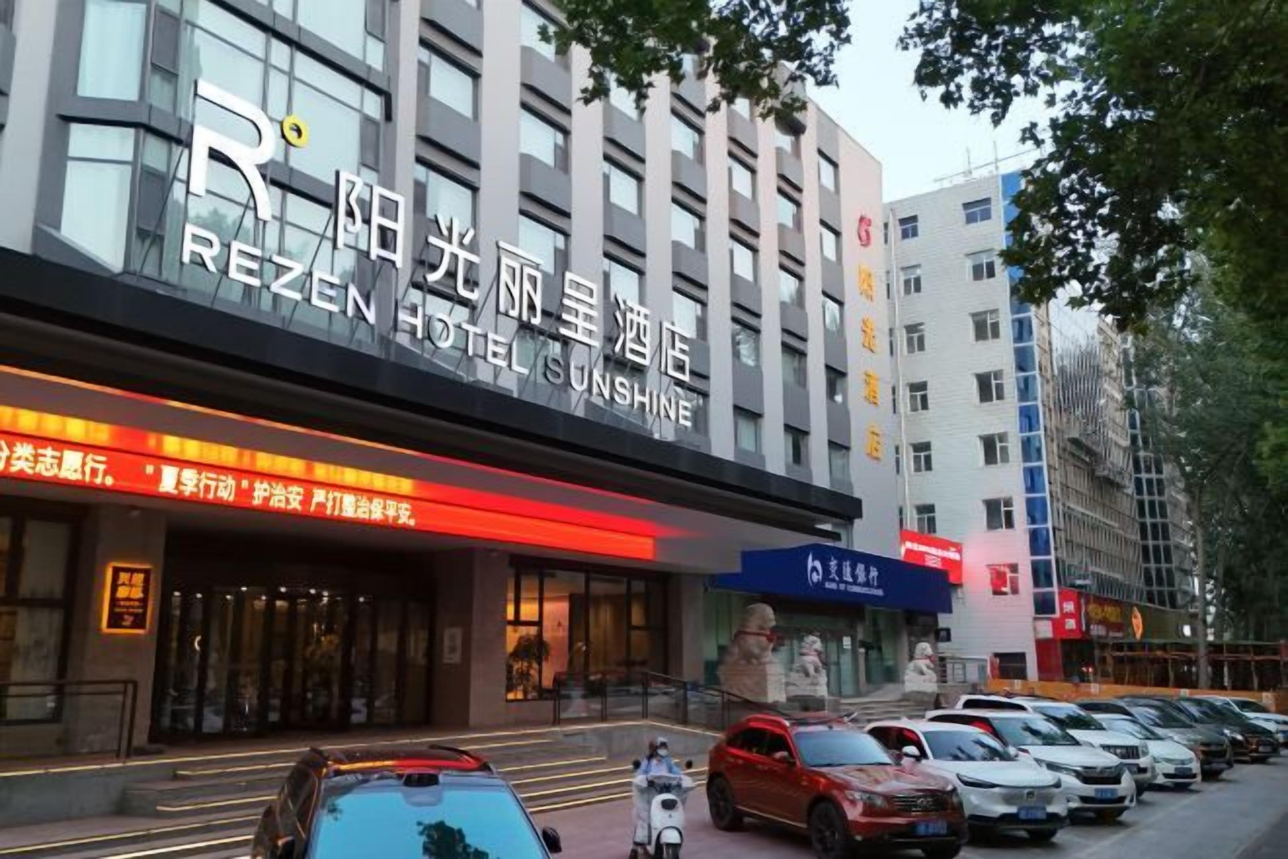 Un hotel con una fachada moderna, una entrada visible y una fila de coches estacionados al frente.