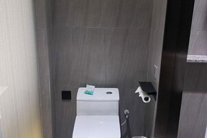 Un baño pequeño y cerrado con inodoro, secamanos y dispensador de toallas de papel.