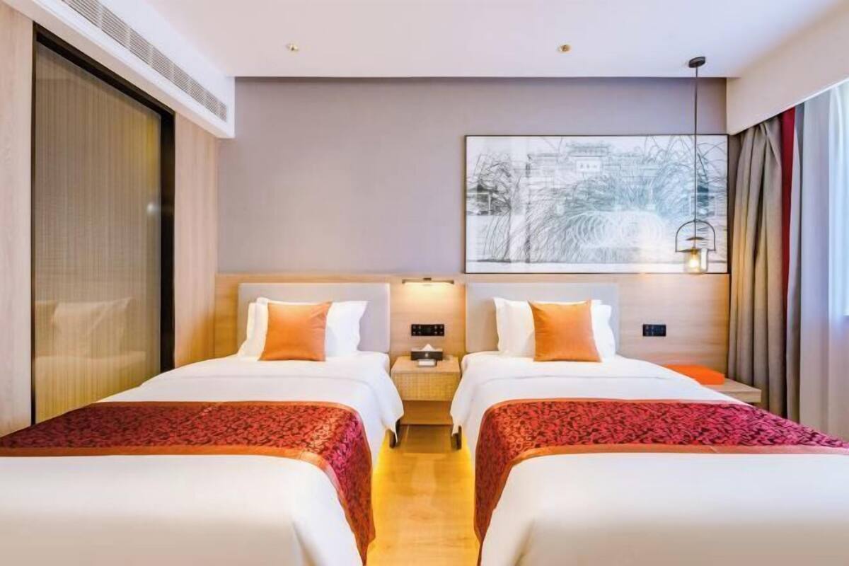 Ett hotellrum med två sängar, ett stort fönster, ett konstverk som hänger på väggen och ett sängbord med en lampa.