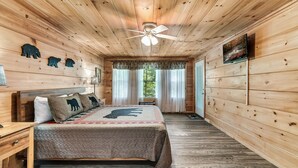 A wooden cabin bedroom with a bed, a nightstand, a ceiling fan, and a window with curtains. -  Dog Friendly w/flat lot - Between Gatlinburg and Pigeon Forge! (Sevierville)