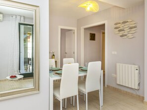A dining area with a table set for four, white chairs, a mirror, and a wall-mounted radiator. - Apartment Mitsu by Interhome (Tossa de Mar)