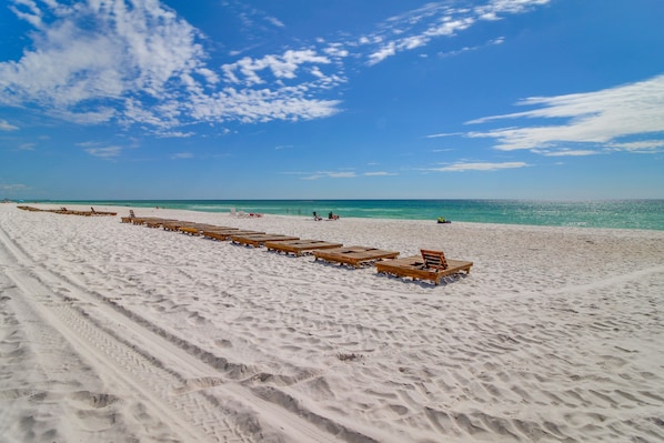 A beach with wooden lounge chairs aligned in rows, a clear blue sky, and a calm sea.