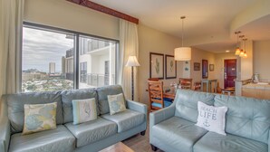 Uma sala de estar moderna com dois sofás de couro azul claro, uma mesa de jantar de madeira e vista para o horizonte urbano através de grandes janelas.