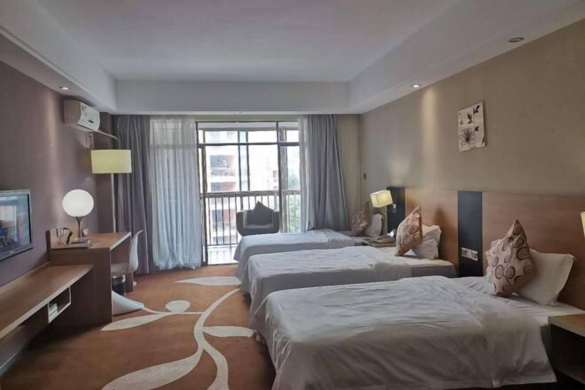 Hotellihuone, jossa on kaksi sänkyä, työpöytä, tuoli, televisio ja suuri ikkuna, jossa on verhot.