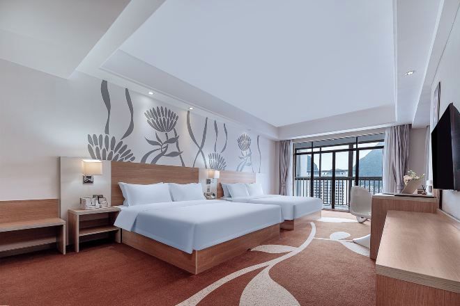Habitación de hotel con dos camas, un escritorio, una silla y un ventanal con vistas.