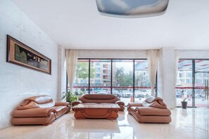 Un hall d’hôtel moderne avec des canapés en cuir, une grande fenêtre donnant sur la ville et une œuvre d’art encadrée accrochée au mur.