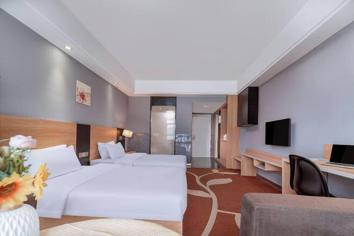 Hotellihuone, jossa on kaksi sänkyä, työpöytä, tuoli, televisio ja pieni pöytä.