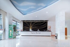 A hotel reception area with a modern design, a reception desk, and a large window. - Yake Hotel (Jingxi)