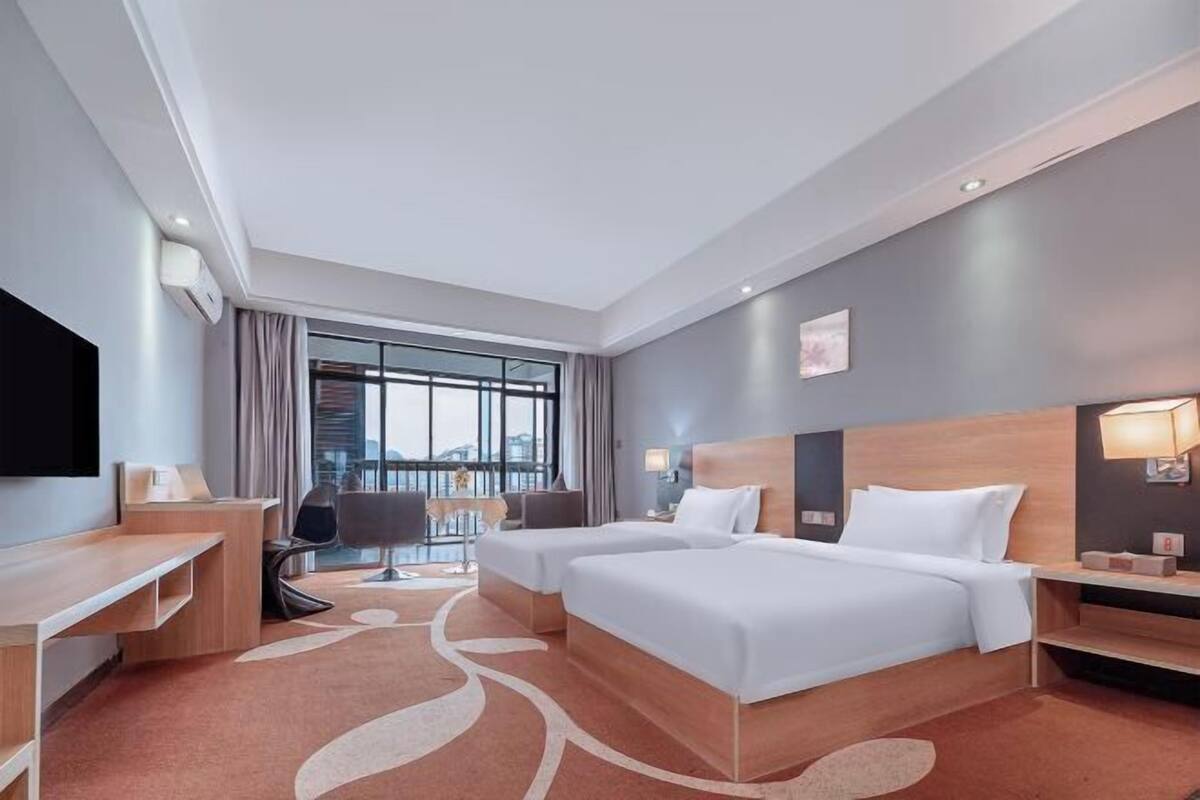 Hotellihuone, jossa on kaksi sänkyä, työpöytä, tuoli, televisio ja suuri ikkuna, jossa on verhot.