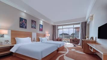 Habitación de hotel con dos camas, un escritorio, televisor y ventana grande con vistas.