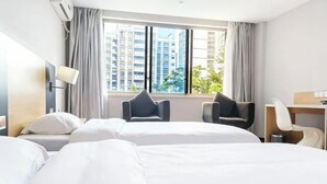 Habitación de hotel con dos camas, un escritorio, una silla y un amplio ventanal con vistas a la ciudad.