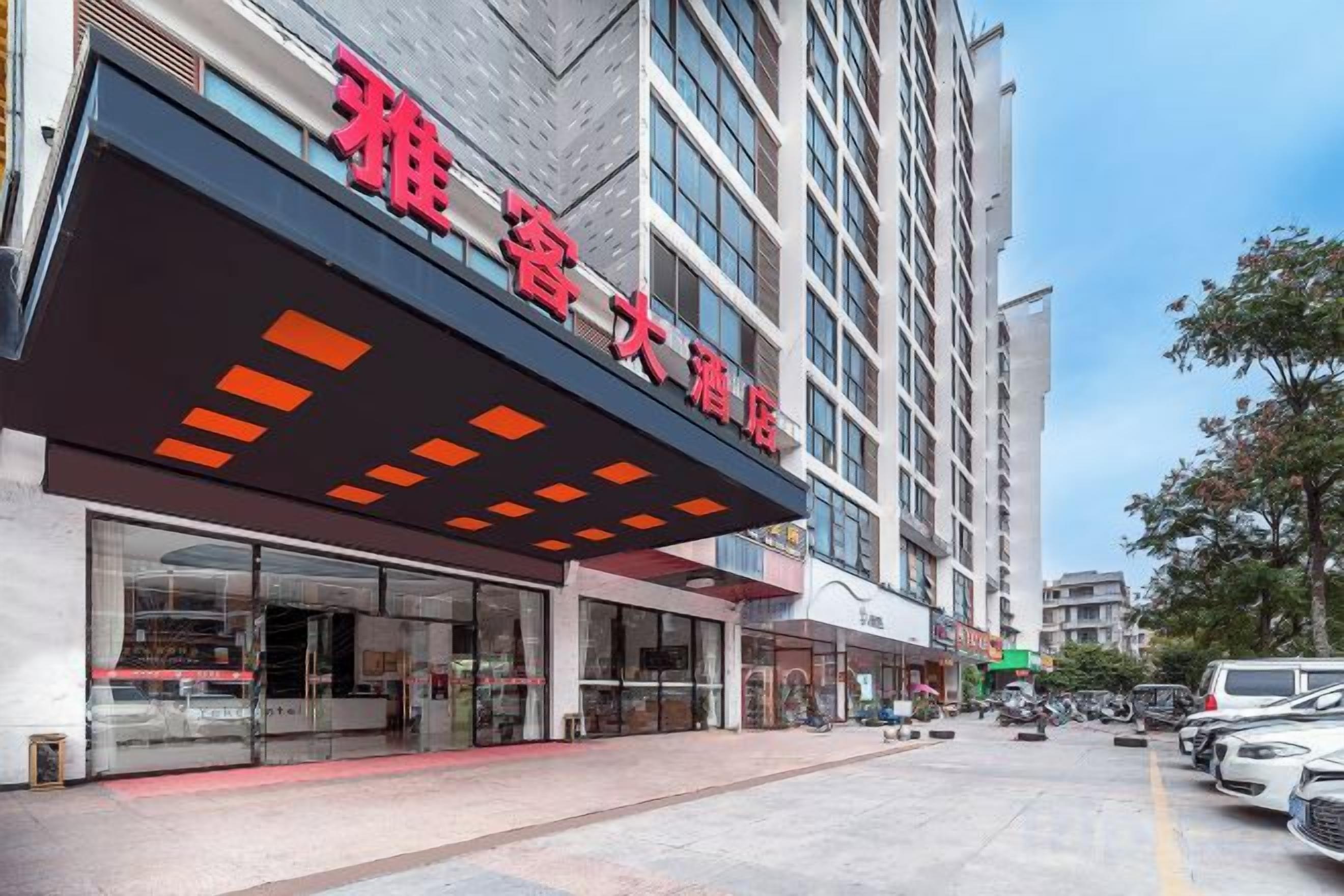 Un hotel con fachada moderna, amplios ventanales y una entrada destacada con toldo rojo.