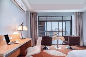 A hotel room with a desk, laptop, two chairs, a lamp, a dining table with a vase, and a large window with curtains. - Yake Hotel (Jingxi)