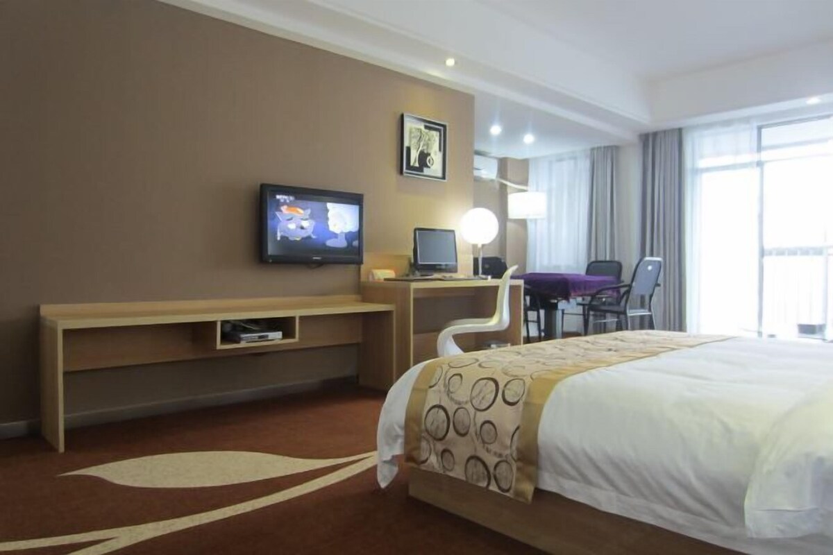 A hotel room with a large bed, a desk with a computer, a TV, and a chair.
