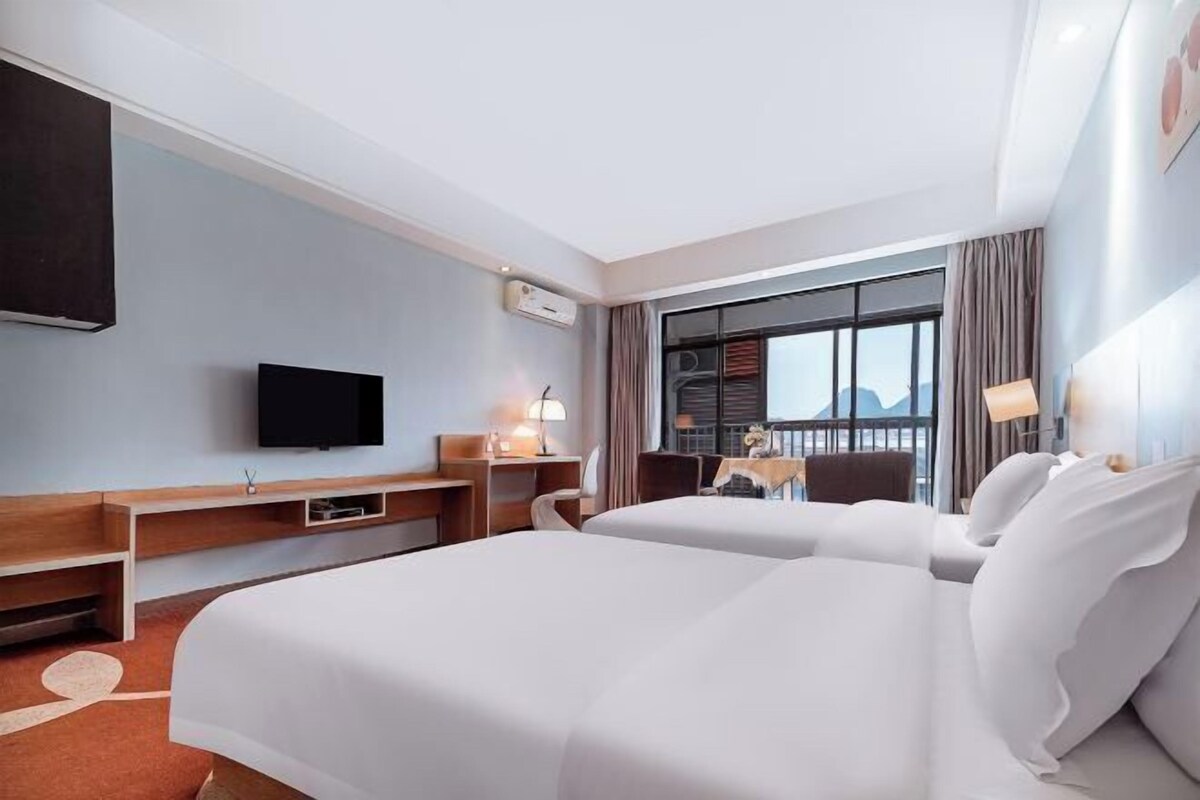 A hotel room with two beds, a TV, a desk, and a balcony with a view.