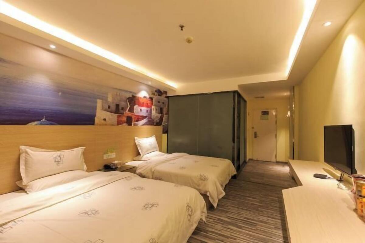 Quarto de hotel com duas camas, televisão, quadro na parede e cabeceira de madeira.