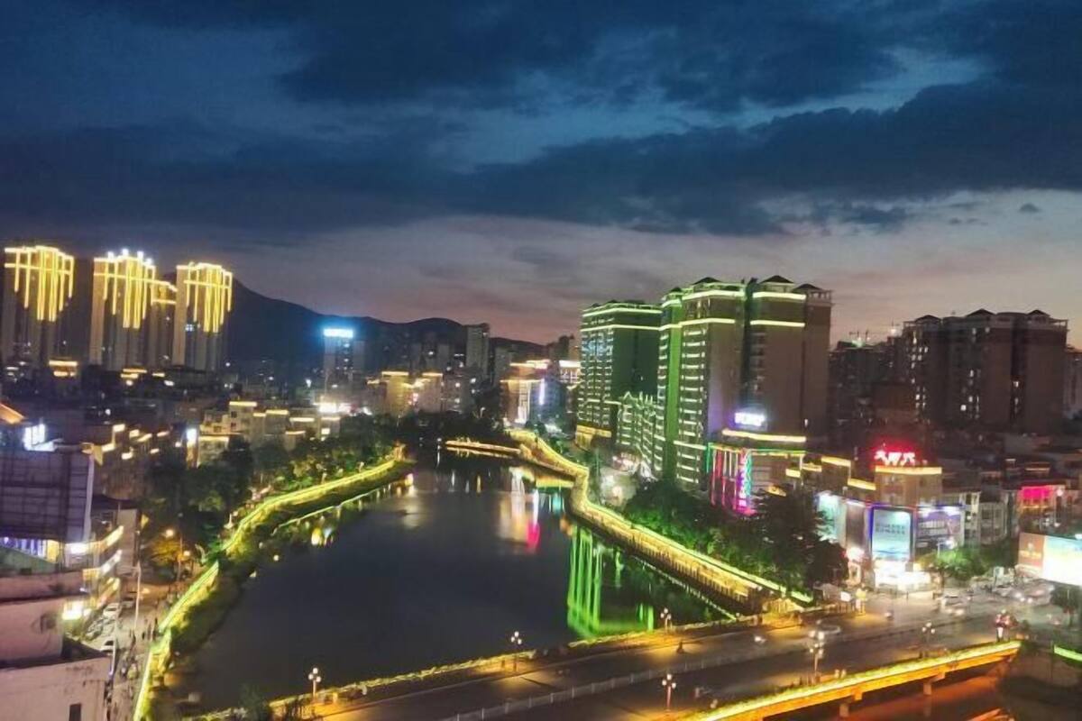 Paisagem urbana noturna com edifícios iluminados, um rio e uma ponte.