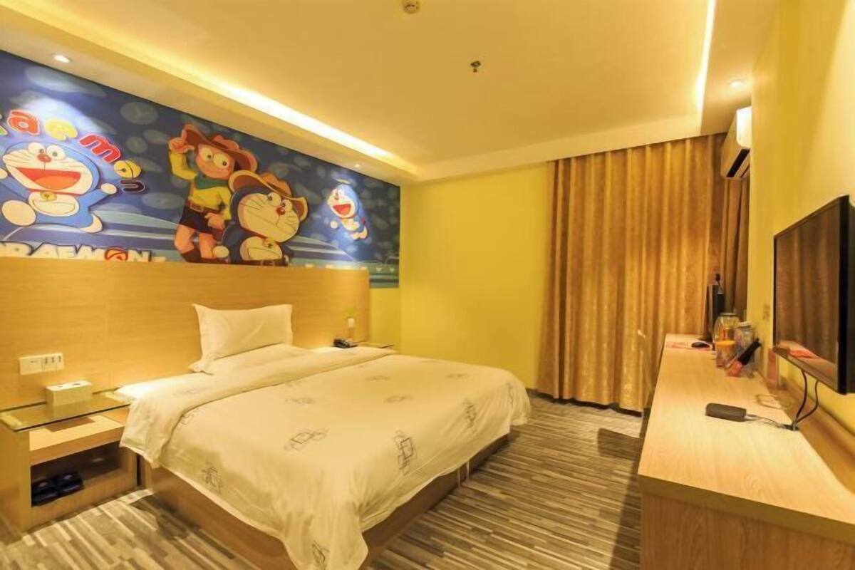 Quarto de hotel com cama, escrivaninha, televisão e um mural na parede.