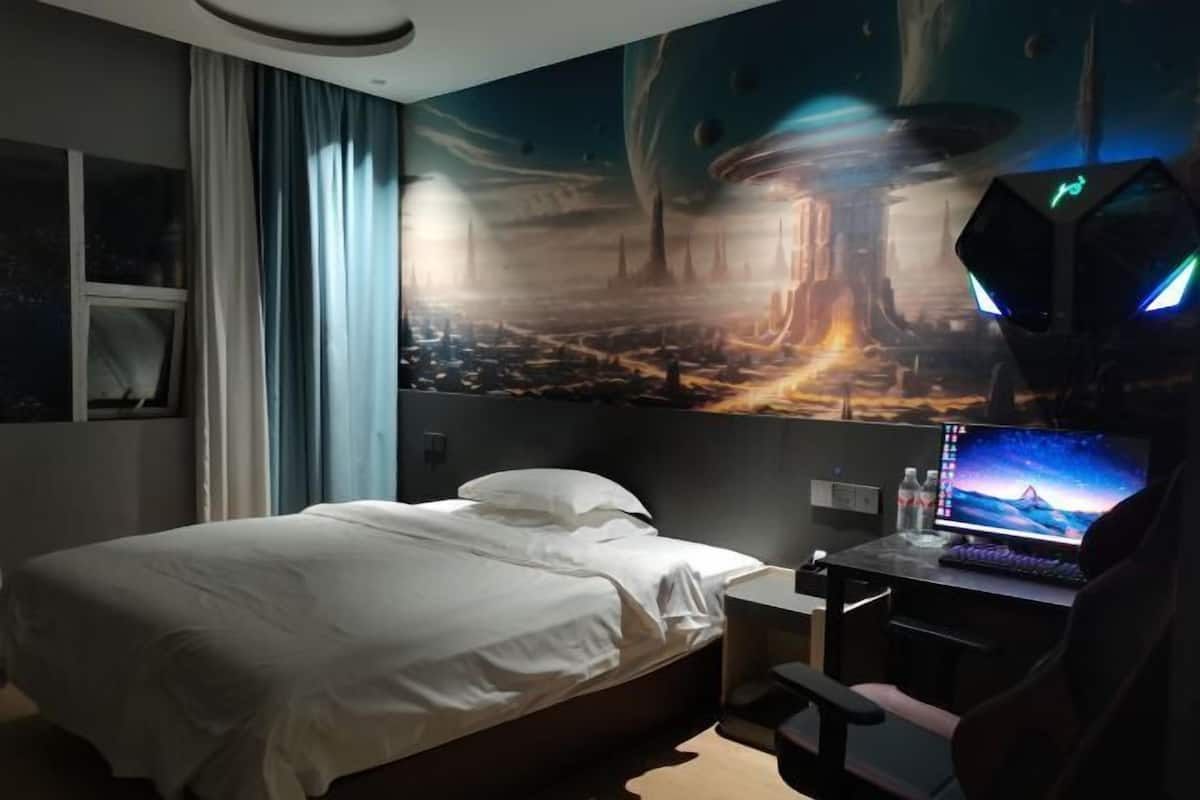 Quarto com cama, escrivaninha com computador e um mural na parede.