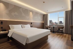 A modern hotel room with a large bed, a city view, a small table, and a chair.