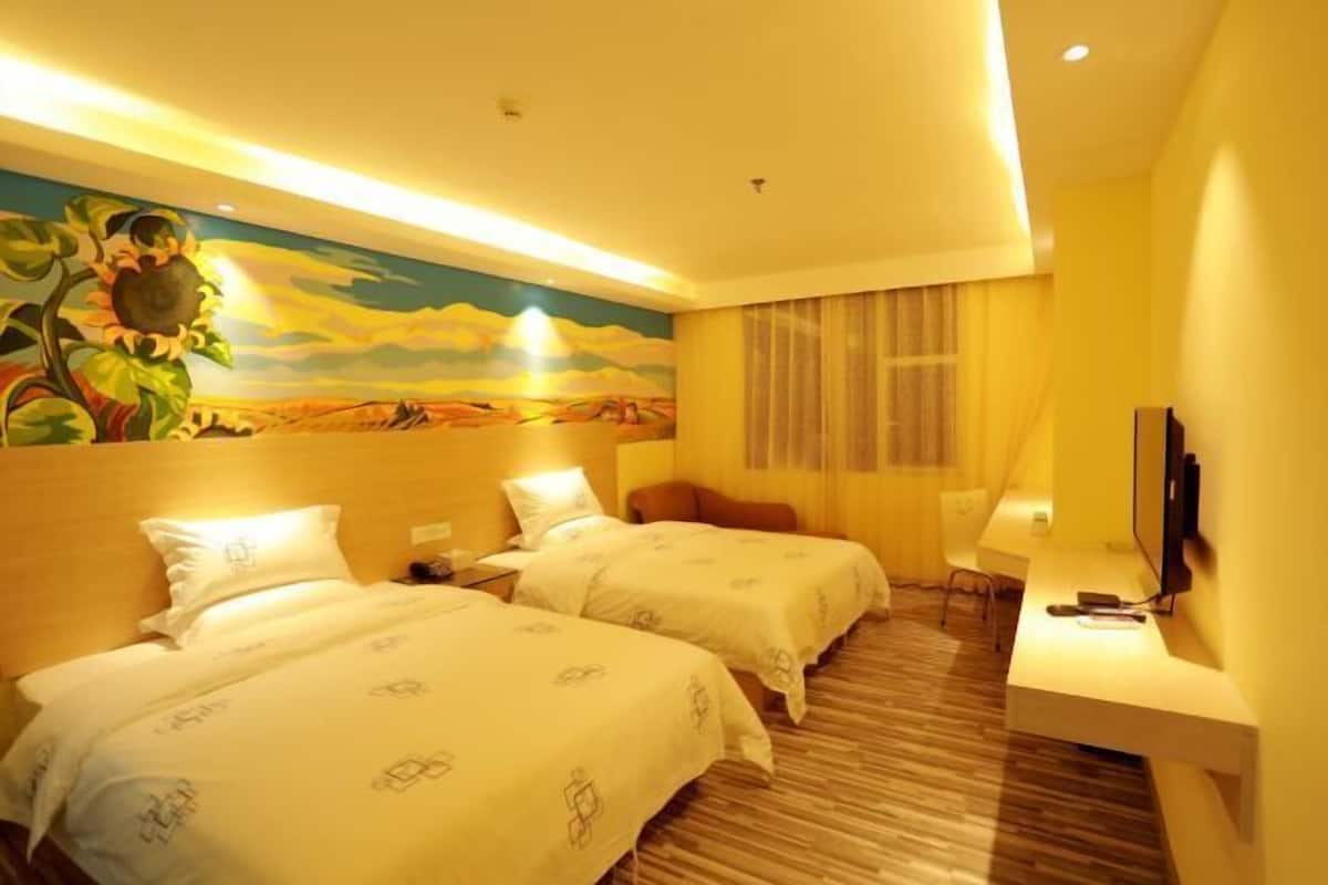 Quarto de hotel com duas camas, uma mesa de trabalho, uma televisão e um mural na parede.
