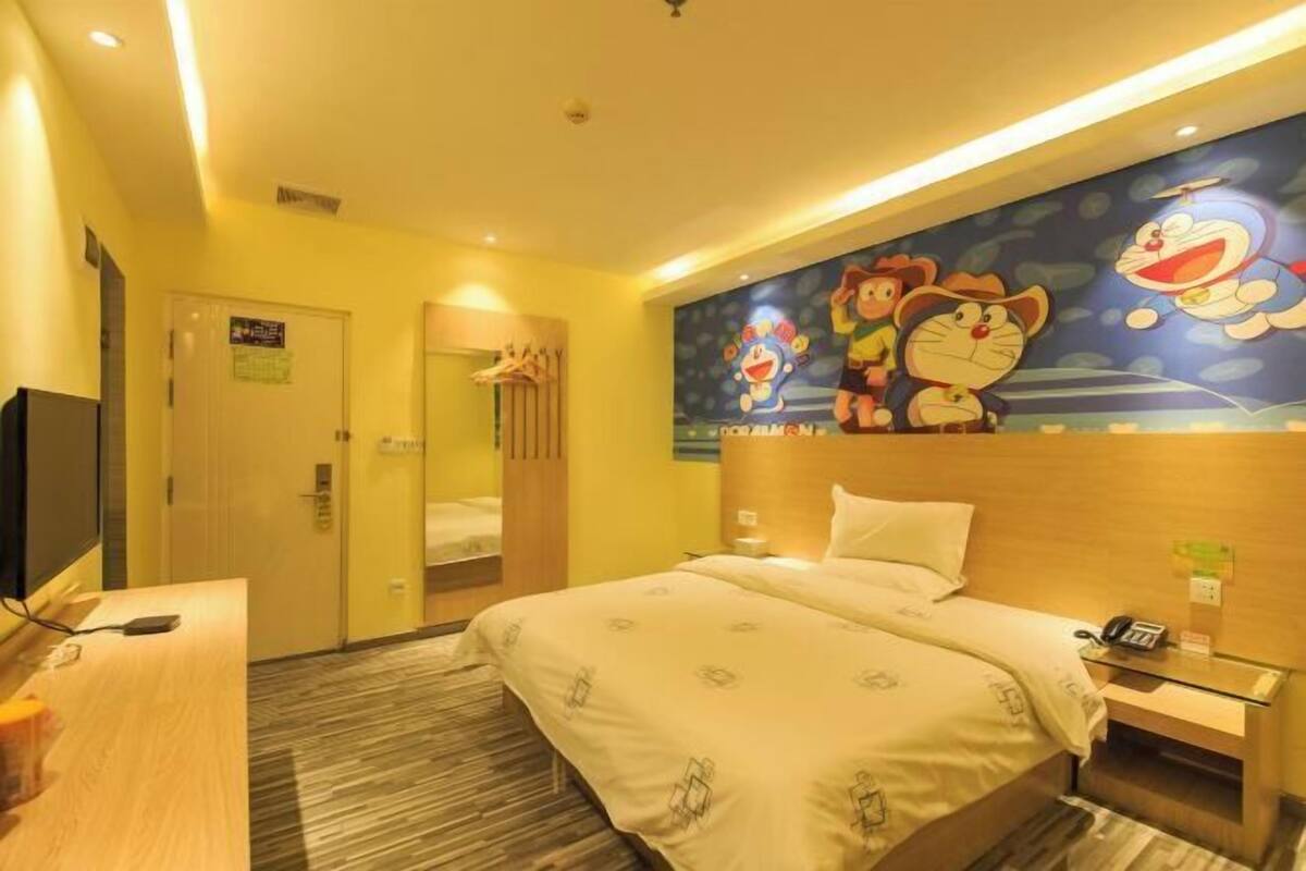 Quarto de hotel com cama, escrivaninha, televisão e parede com personagens de desenho animado.