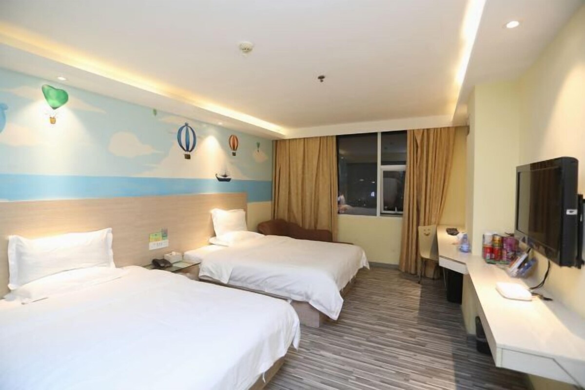 A hotel room with two beds, a desk with a flat-screen TV, a window with curtains, and a wall with a sky-themed mural.