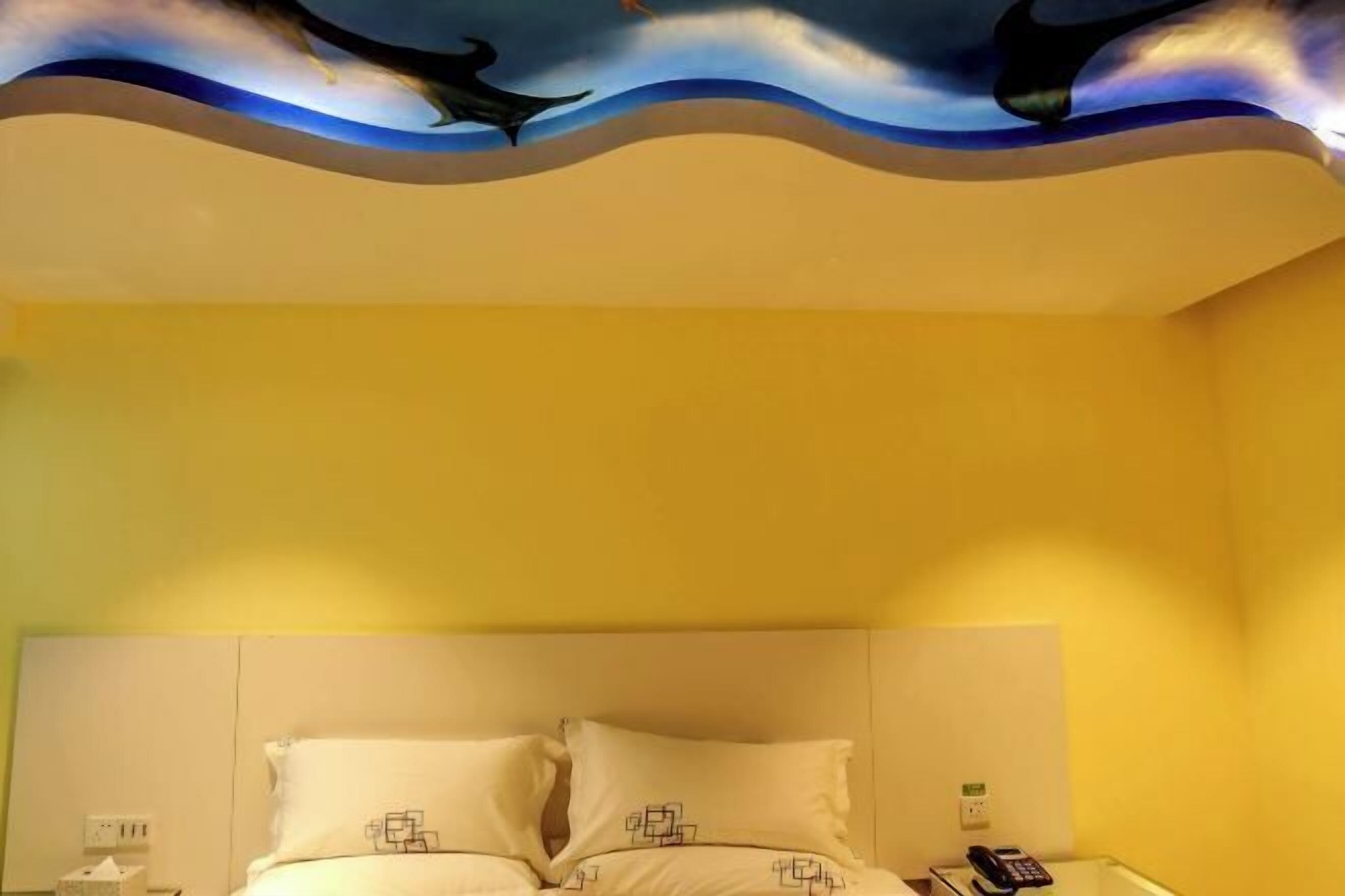 A hotel room with a bed, a bedside table with a telephone, and a wall with a decorative ceiling.