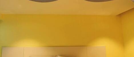 A hotel room with a bed, a bedside table with a telephone, and a wall with a decorative ceiling.