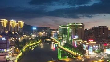 Een verlicht stadsbeeld bij nacht, met gebouwen, een rivier en een brug.