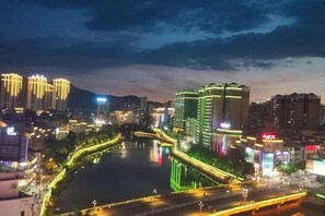 A nighttime cityscape with illuminated buildings, a river, and a bridge. - Siji Hotel (Cenxi)