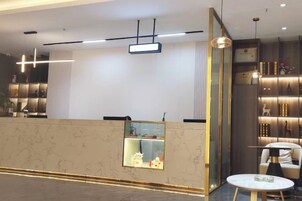 Una moderna recepción con mostrador de mármol, iluminación colgante y una zona de estar con una mesa redonda.
