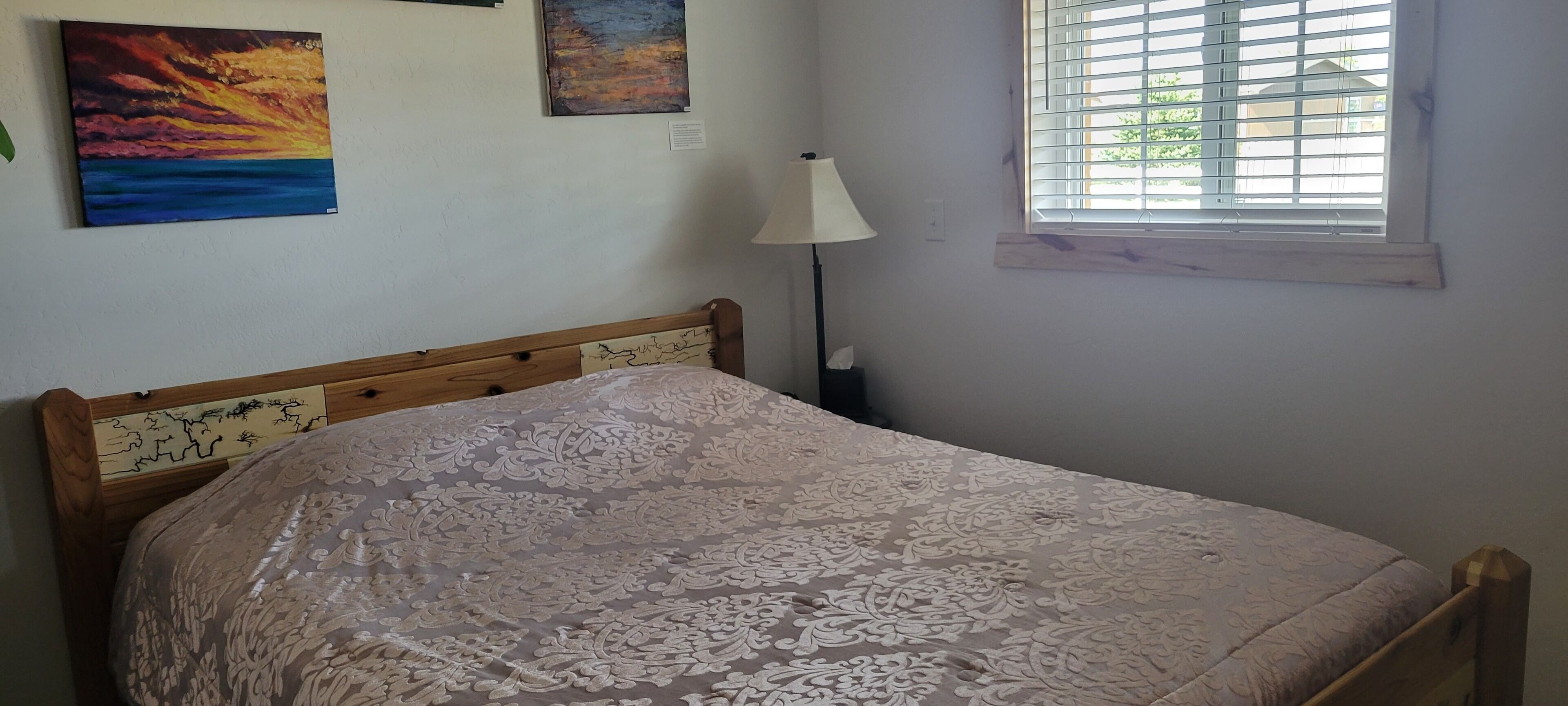 A bedroom with a bed, a nightstand, a lamp, and a window with blinds.