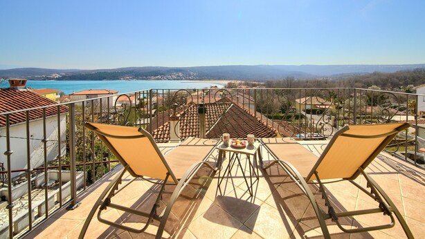 A terrace with two sun loungers, a table with a drink, and a view of a coastal area with buildings and a body of water. - Villa Kate (Kvarner - Čižići) (Čižići)